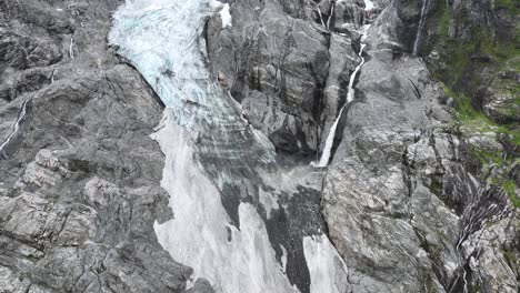 River-stream-of-melted-glacial-ice-is-running-down-mountain-cliffs-beside-tongue-of-Boyabreen-Glacier-in-Fjaerland-Norway---60-fps