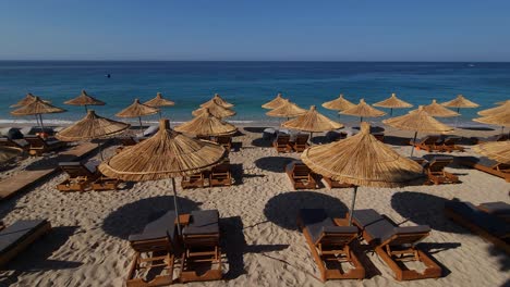 Straw-umbrellas-and-lounges-rows-on-beautiful-beach,-tourist-spot-in-beautiful-coastline-in-Albania