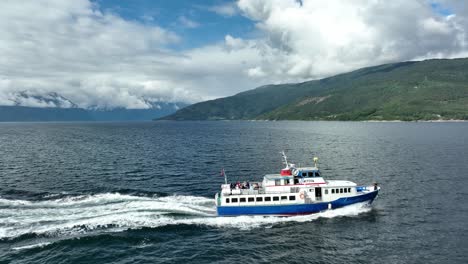 Turistas-Divirtiéndose-A-Bordo-De-Un-Barco-Turístico-En-Sognefjorden,-Noruega---Antena-Desde-El-Costado-Del-Barco-Moviéndose-Hacia-Arriba-Y-Girando-Hacia-El-Paisaje-Montañoso