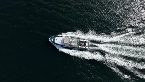 Private-tourist-charter-boat-sailing-at-the-Sognefjorden-in-Norway---Aerial-moving-upwards-and-tilting-down-into-birdseye-view-above-boat-with-people-on-aft-deck