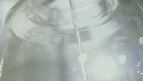 Close-up-shot-of-distilled-alcohol-flowing-inside-a-glass-jar,-industrial-process-in-a-gin-distillery-production