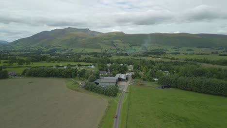 Flying-over-farm-and-campsite-towards-mountain-Blencathra-on-cloudy-summer-day