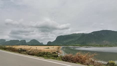 Fahren-Entlang-Einer-Straße-Neben-Einem-See-Mit-Bergigen-Hügeln-Im-Hintergrund-In-Thailand