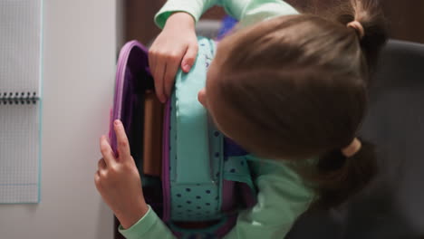 Little-girl-opens-schoolbag-sitting-at-desk-in-classroom