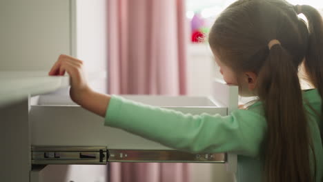 Curious-little-girl-opens-desk-drawer-in-children-room