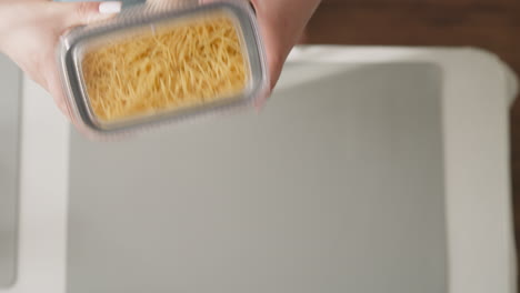 Frau-Schüttelt-Behälter-Mit-Spaghetti-über-Dem-Tisch