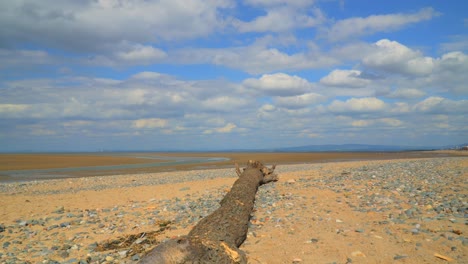 Clouds-drifting-by-over-beach-with-large-driftwood-tree-trunk