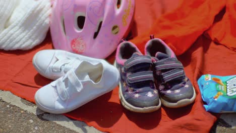 Ein-Paar-Lila-weiße-Kinderschuhe-Und-Ein-Rosafarbener-Fahrradhelm-Auf-Einem-Flohmarkt