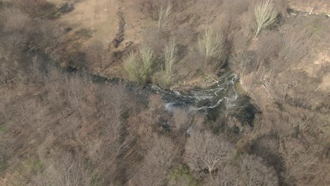 Drone-aerial-of-a-river-flowing-through-a-wooded-area-in-winter