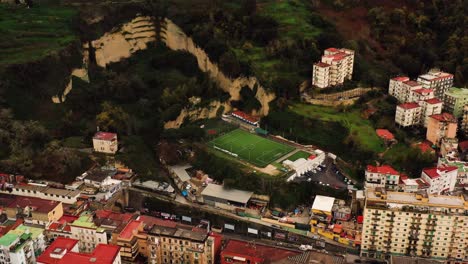 Aerial-orbit-shot-of-soccer-field-on-hilltop-surrounded-by-city-of-Naples-in-Italy