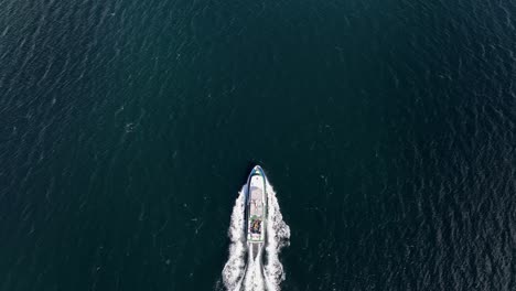Tourist-charter-boat-coming-into-frame-and-moving-ahead-in-this-static-birdseye-aerial---Sognefjorden-sea-in-western-Norway-60-fps
