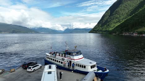 Touristisches-Ausflugsboot,-Das-Von-Vik-In-Sogn,-Norwegen,-Abfährt-–-Sommerkreuzfahrt-Mit-Fjordlandschaftshintergrund-Und-Bus,-Der-Am-Kai-Zurückgelassen-Wird,-Während-Der-Busfahrer-Mit-Der-Hand-Winkt