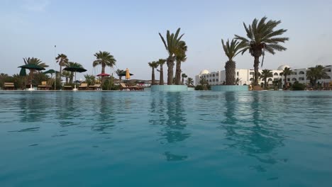 Low-angle-water-surface-POV-of-swimming-pool-of-luxury-holiday-resort-in-Tunisia-at-sunset-on-windy-day