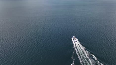 High-angle-aerial-view-of-motorboat-sailing-the-famous-Sognefjorden-towards-Balestrand-Norway---Tilt-up-from-isolated-boat-on-sea-to-view-towards-Balestrand-with-beautiful-landscape---60-Fps