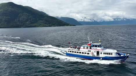 Aerial-passing-right-over-happy-tourists-on-deck-of-Norway-sightseeing-boat---Sognefjorden-sea-Aerial-60-fps