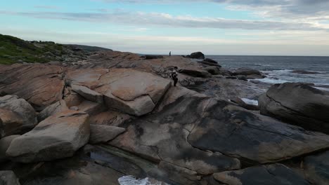 Frau-Geht-Und-Sitzt-Auf-Den-Felsen-Des-Red-Gate-Beach-Mit-Blick-Auf-Das-Meer-Bei-Sonnenuntergang,-Westaustralien