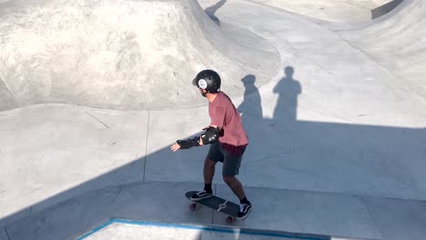 Professional-skater-in-bowl-skatepark-doing-tricks,-skateboarder-carving-a-turn-in-a-deep-concrete-bowl,-young-man-on-extreme-surfboard-in-sunny-day