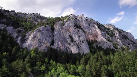 Tilt-up-reveal-of-cliff-mountain-range-surrounded-by-forest-in-the-summer