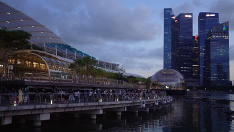 People-take-photos,-walk-outside-the-waterfront-and-against-the-futuristic-Apple-flagship-retail-store-and-the-skyscrapers-in-Marina-Bay,-Singapore
