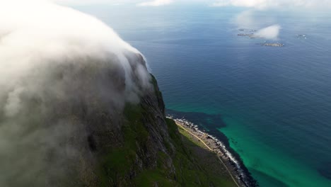 Aerial-view-of-clouds-covering-the-mountains-with-Uttakleiv-beach-beneath-it-in-Lofoten,-Norway