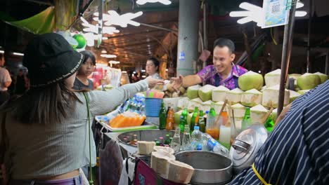 Una-Mujer-Entrega-El-Pago-Al-Vendedor-Por-El-Jugo-De-Coco,-Mientras-El-Hombre-De-La-Derecha-Coloca-Los-Cocos-Fríos-Abiertos-En-El-Contenedor.