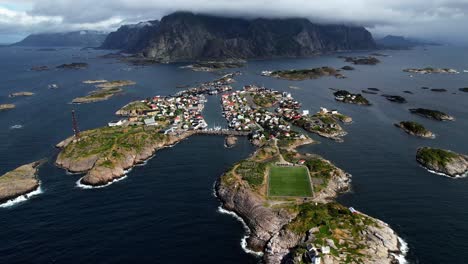 Aerial-of-the-beautiful-football-field-in-Lofoten,-Norway-with-the-city-of-Henningsvaer-and-mountains-behind-it-in-Lofoten,-Norway