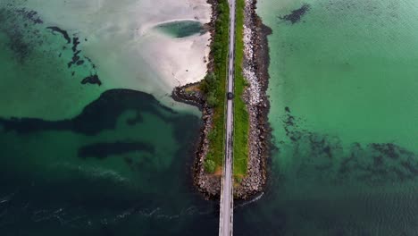 Aerial-view-of-a-car-driving-on-a-bridge-in-the-beautiful-landscape-of-Lofoten,-Norway