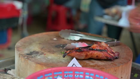 A-busy-street-hawker-at-Chatuchak-Weekend-Market,-serving-food-from-the-right,-getting-orders,-and-chopping-grilled-chicken-to-serve-to-the-next-customer-in-Thailand's-famous-night-market