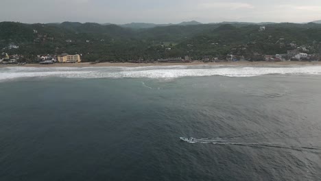 Aerial-view:-Ocean-boat-motors-just-off-misty-sand-beach,-Mazunte-MX