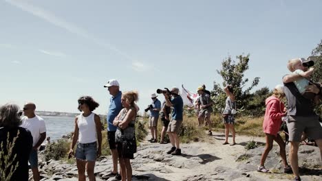 People-of-all-ages-gather-on-rocks-by-the-ocean-watching-a-sailing-event
