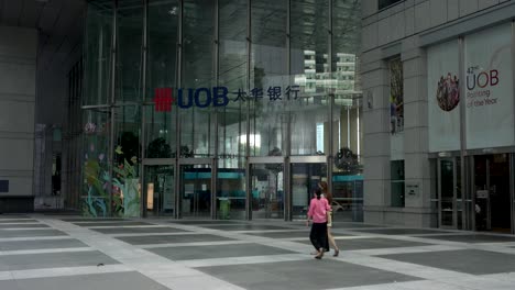 People-saunter-outside-the-entrance-of-the-UOB-Building,-a-blend-of-modern-architecture-and-timeless-elegance-at-Raffles-Place,-an-iconic-landmark-in-Singapore's-central-business-district