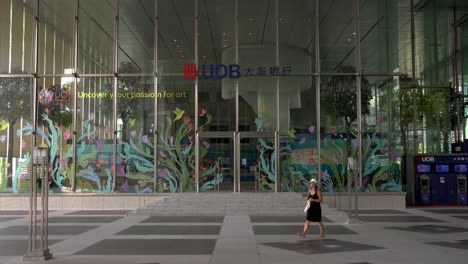 Woman-saunters-outside-the-entrance-of-the-UOB-Building-at-Raffles-Place,-a-financial-district-in-the-heart-of-Singapore's-Central-Business-District-