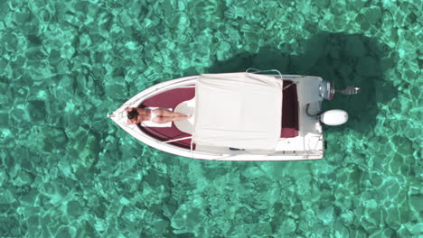 Birdseye-Aerial-View-of-Woman-in-Topless-Sunbathing-on-Bow-of-Motor-Boat-in-Crystal-Clear-Turquoise-Sea-Water
