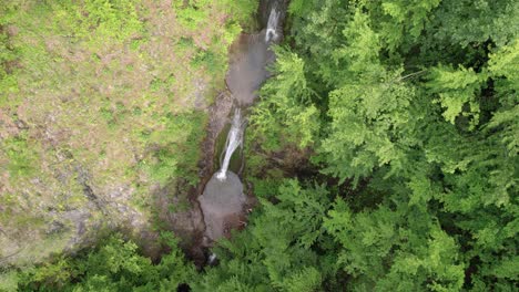 High-up-view-of-a-double-waterfall-in-a-forest,-rotating-drone-shot