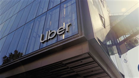 Tilt-down-to-Uber-company-signage-on-sunlit-glass-front-California-headquarters-exterior-building