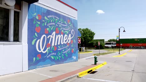 Mural-En-El-Centro-De-Ames,-Iowa,-Con-Tren-Moviéndose-A-Distancia-Y-Vídeo-Estable.