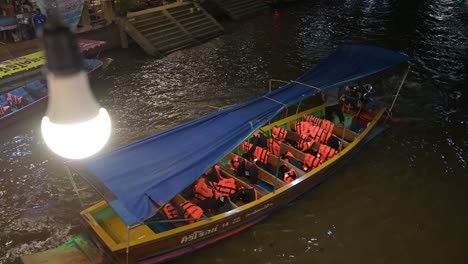 Un-Barquero-Solitario-Dirige-Un-Barco-De-Madera-Vacío-Hacia-La-Parte-Superior-Derecha-Del-Marco,-En-El-Canal-Del-Mercado-Flotante-De-Amphawa,-Samut-Songkhram,-Tailandia