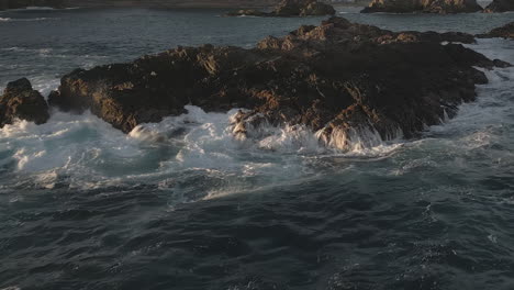 Low-angle-golden-sunset-lights-ocean-waves-crashing-onto-jagged-rocks
