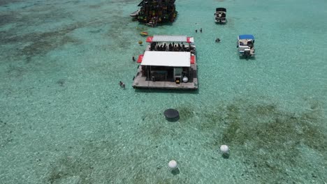 Jóvenes-Disfrutando-Bailando-En-Medio-Del-Mar-Caribe,-En-Una-Isla-De-Madera-Flotante,-Drone-4k