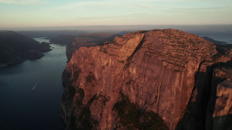 Stunning-Aerial-View-of-a-Sunrise-Atmosphere-in-the-Lysefjorden,-A-Boat-is-Cruising-on-the-Sea,-Preikestolen,-Pulpit-Rock,-Norway