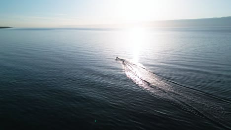 Experience-the-thrill-of-a-jetski-gliding-along-the-Baltic-Sea-shore-at-sunset,-captured-in-stunning-detail-by-a-drone