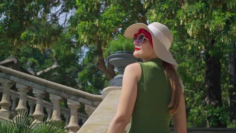 Stunning-footage-of-a-girl-in-a-green-dress-with-hat-walks-up-the-stairs,-joyfully-observing-Cascada-Monumental-Gaudí's-fountain-and-Parc-de-la-Ciutadella