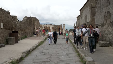Eine-Zeitlupenaufnahme-Eines-Reiseleiters,-Der-Sein-Wissen-über-Die-Gegend-Weitergibt,-Während-Die-Touristengruppe-Eine-Alte-Straße-Entlang-Geht,-Die-Von-Ruinen-In-Pompeji,-Italien,-Umgeben-Ist