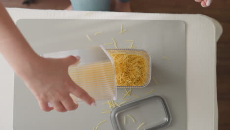 Woman-pours-spaghetti-and-covers-plastic-container-with-lid
