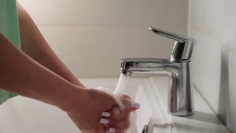 Frau-öffnet-Wasserhahn-Und-Wäscht-Hände-über-Weißem-Waschbecken