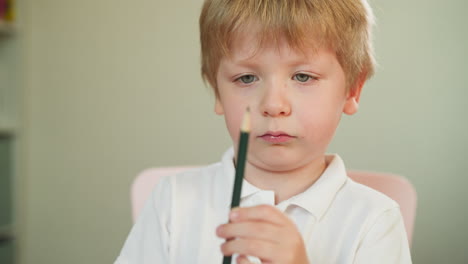 Serious-toddler-boy-studies-green-crayon-pencil-in-hands