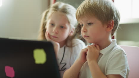 Toddler-boy-and-schoolgirl-look-at-computer-sitting-at-table