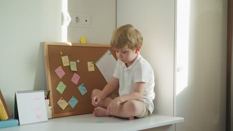 Barefoot-toddler-examines-piece-of-paper-with-note-holding-pin
