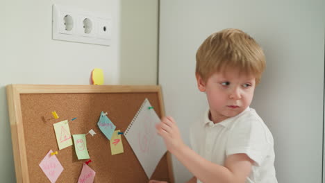 Toddler-boy-attaches-note-to-board-playing-with-stationery