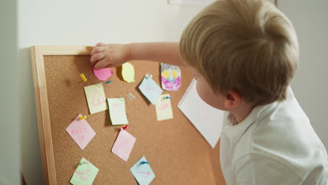 Toddler-boy-presses-pink-paper-figure-to-cork-board